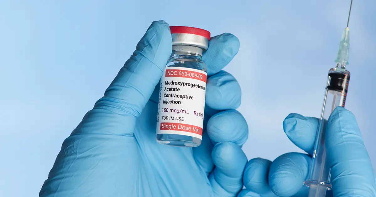 Depo-Provera contraceptive injection (Medroxyprogesterone Acetate) in a single-dose vial, held by gloved hands with a syringe.