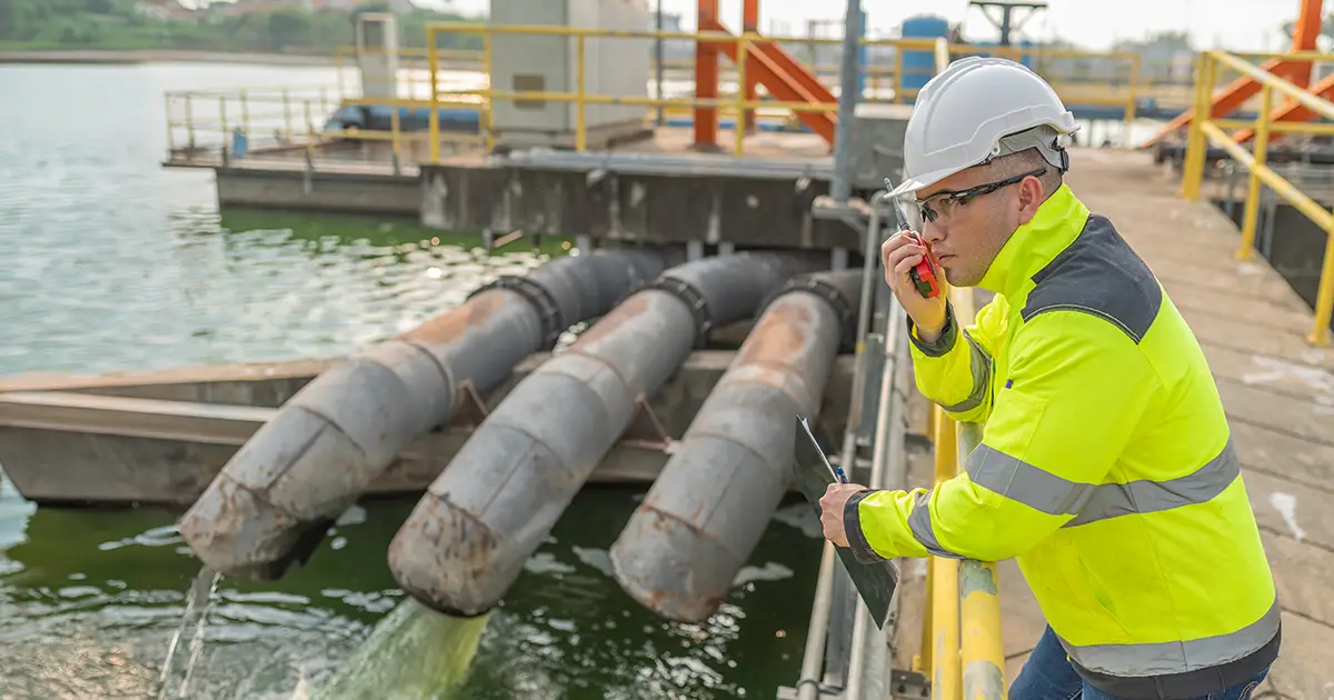 Industrial worker in a hard hat near water discharge pipes, indicating PFAS exposure risk
